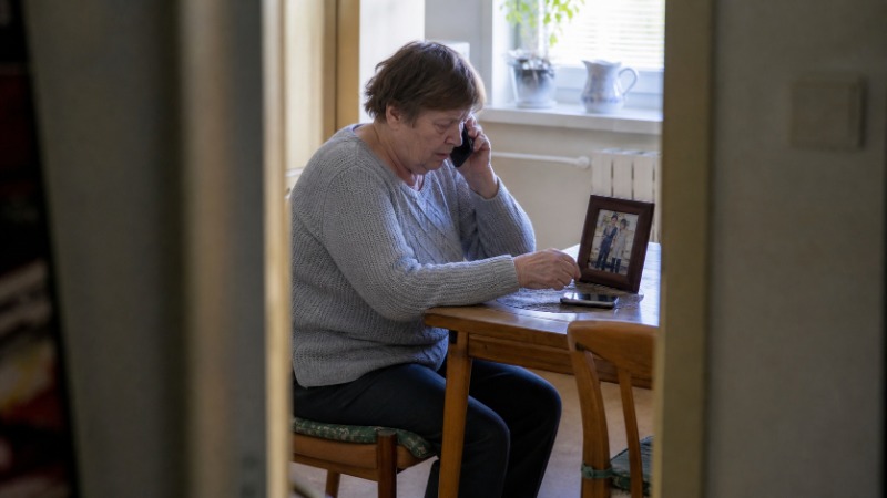 Starší žena drží telefon a s obavami si zapisuje poznámky na papír