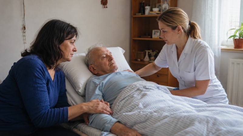 Zdravotní sestra domácího hospice hovoří s pacientem a jeho dcerou v obývacím pokoji